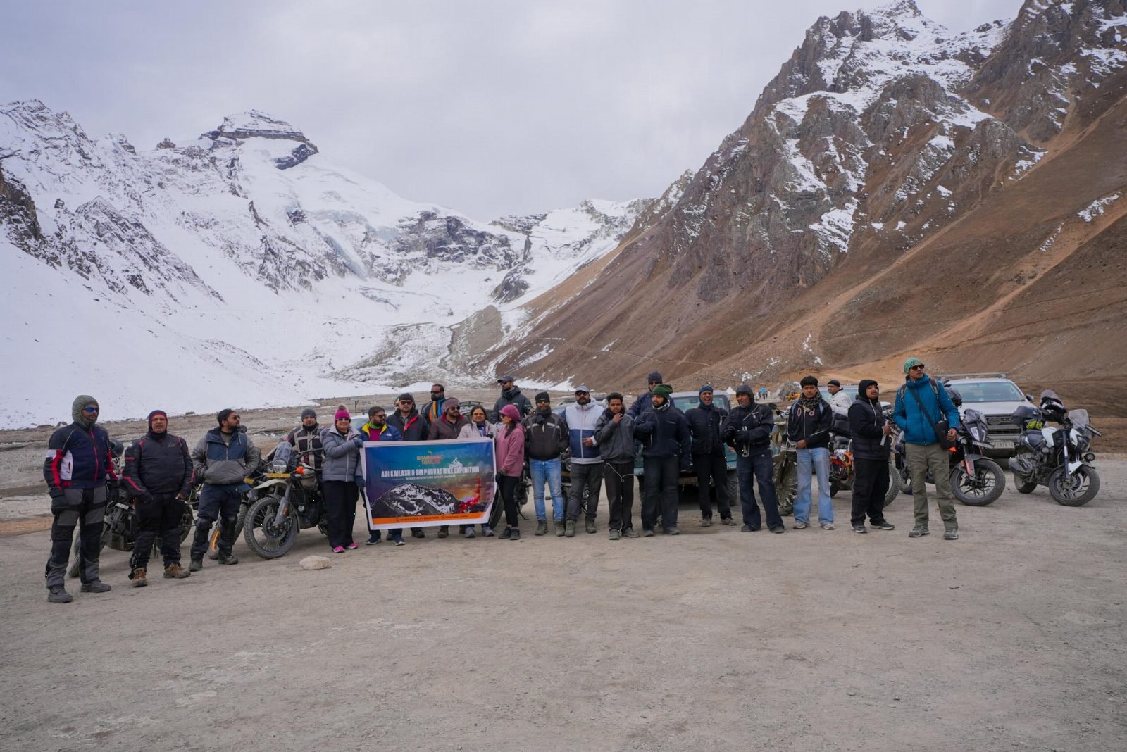 Brahmanic Trailss riders with the Adi Kailash & Om Parvat Bike Expedition banner beneath snow-covered peaks